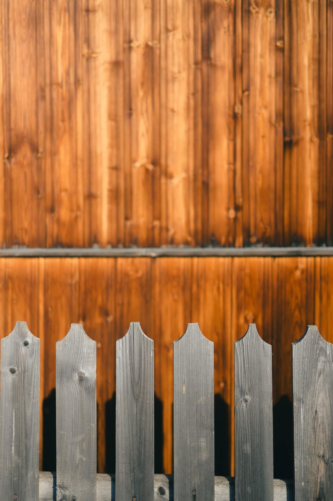 Close-up of a rustic gray wooden fence contrasting against a warm cedar wall in soft natural light.